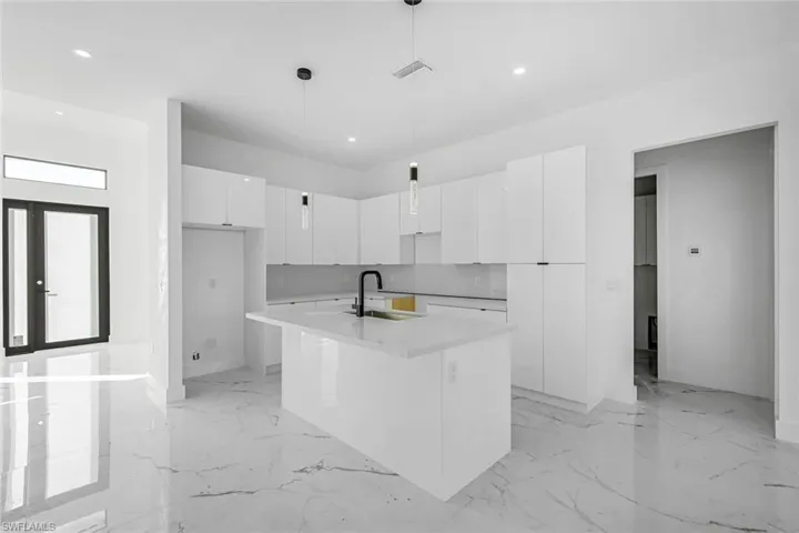 Kitchen with modern cabinets, light marble finish floors, white cabinetry, an island with sink, and recessed lighting