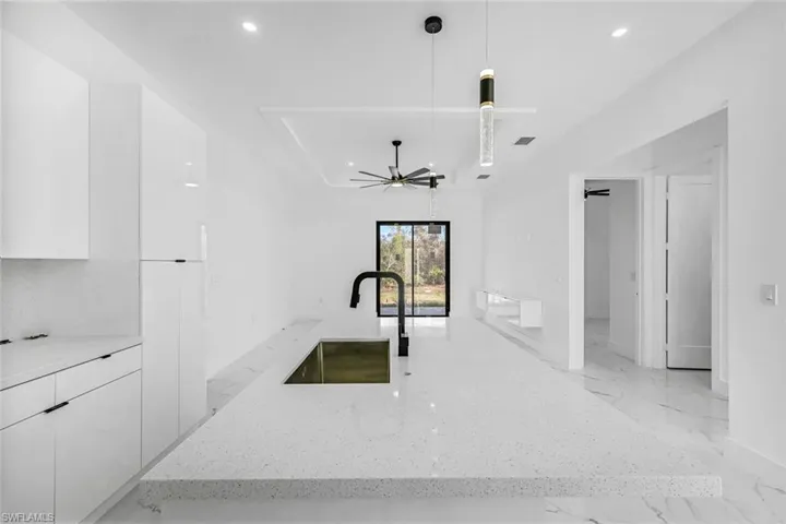 Kitchen with modern cabinets, white cabinets, recessed lighting, pendant lighting, and light stone countertops