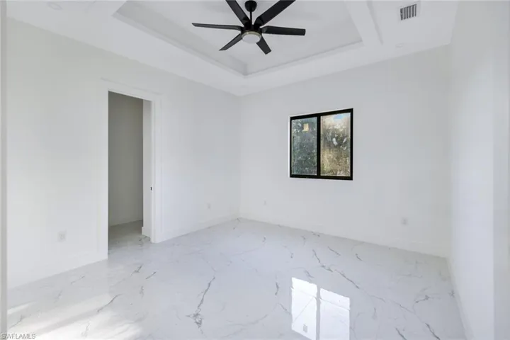 Empty room with a raised ceiling, ceiling fan, and marble finish flooring