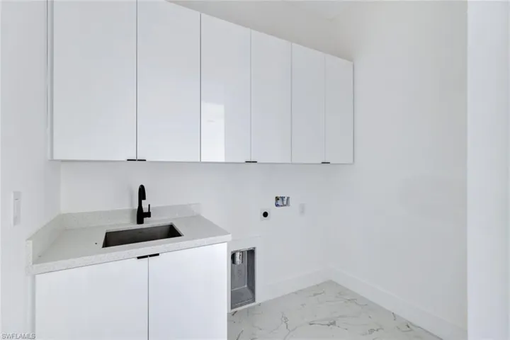 Washroom with hookup for an electric dryer, cabinet space, hookup for a washing machine, and light marble finish flooring