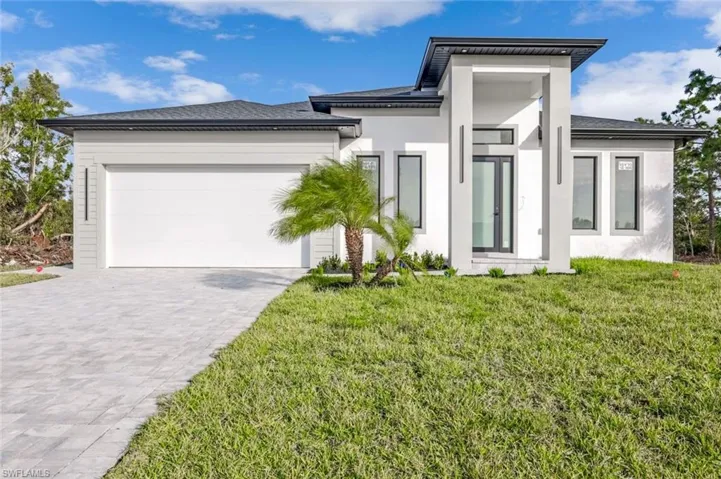 View of front of house featuring decorative driveway, an attached garage, stucco siding, and a front yard
