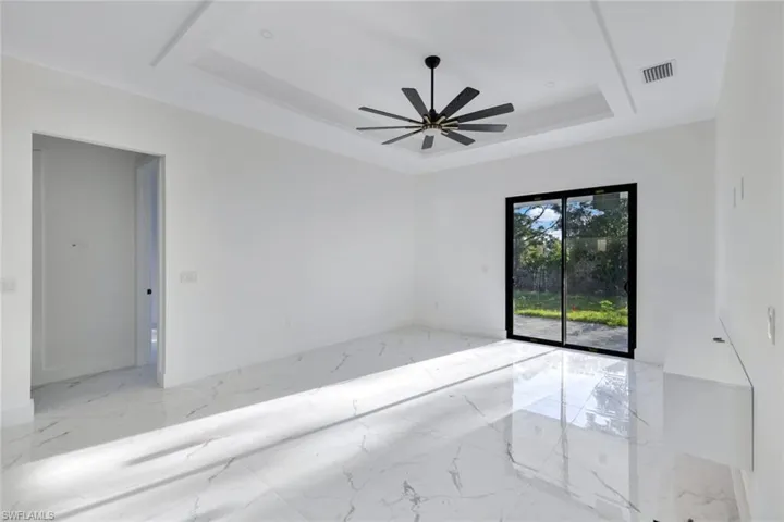 Empty room featuring a raised ceiling, marble tiled flooring, and ceiling fan