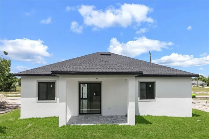 Back of property featuring roof with shingles, stucco siding, and a lawn