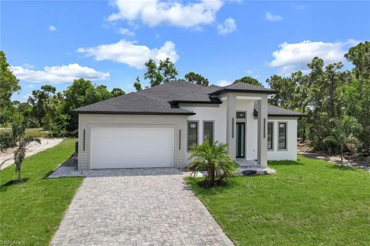 Prairie-style house with a garage, stucco siding, decorative driveway, and a front lawn