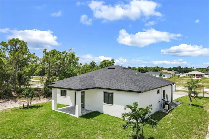 Back of house featuring a lawn, stucco siding, and roof with shingles