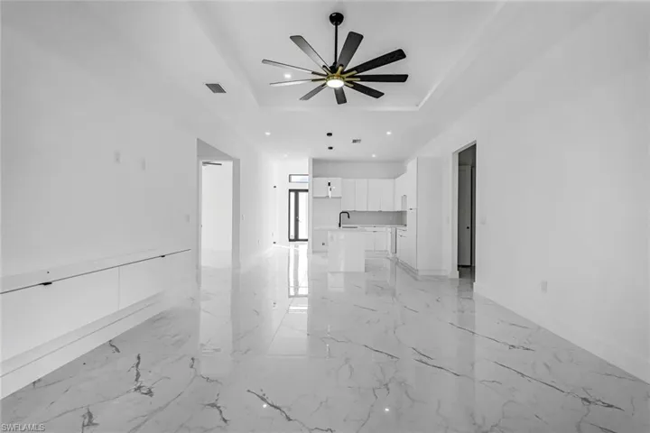 Unfurnished living room with a raised ceiling, light marble finish floors, recessed lighting, and ceiling fan