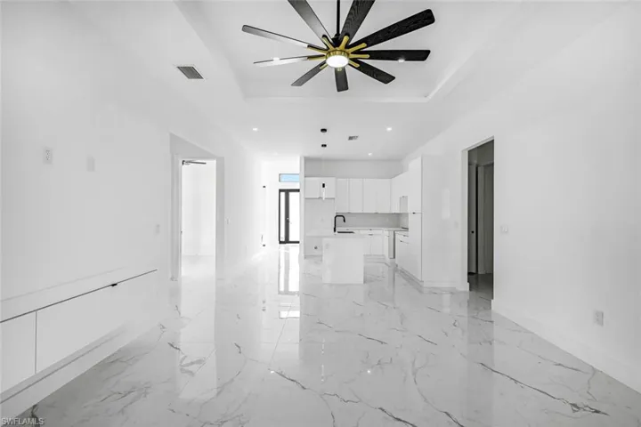 Unfurnished living room with a tray ceiling, ceiling fan, light marble finish flooring, and recessed lighting