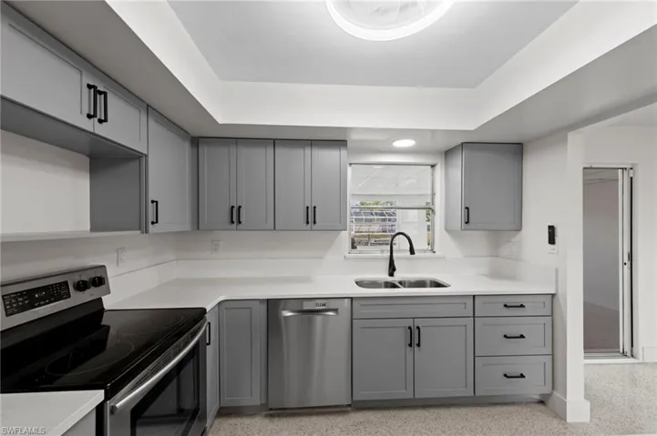 Kitchen featuring gray cabinetry, appliances with stainless steel finishes, dark speckled floor, and light stone countertops