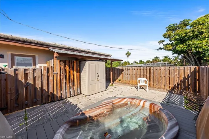 patio with wood fence with a storage unit, a fenced backyard, an outdoor hot tub, and a patio