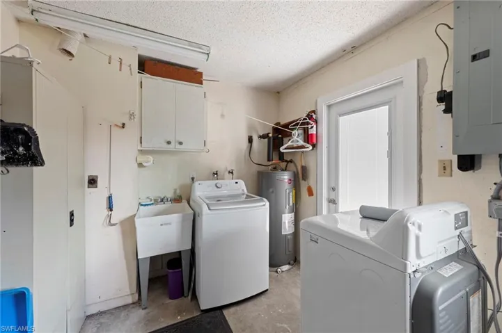 Laundry room featuring electric panel, cabinet space, unfinished concrete flooring, a textured ceiling, and electric water heater