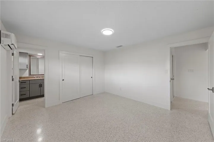 Bedroom featuring a closet, connected bathroom, a wall mounted AC, and dark speckled floor