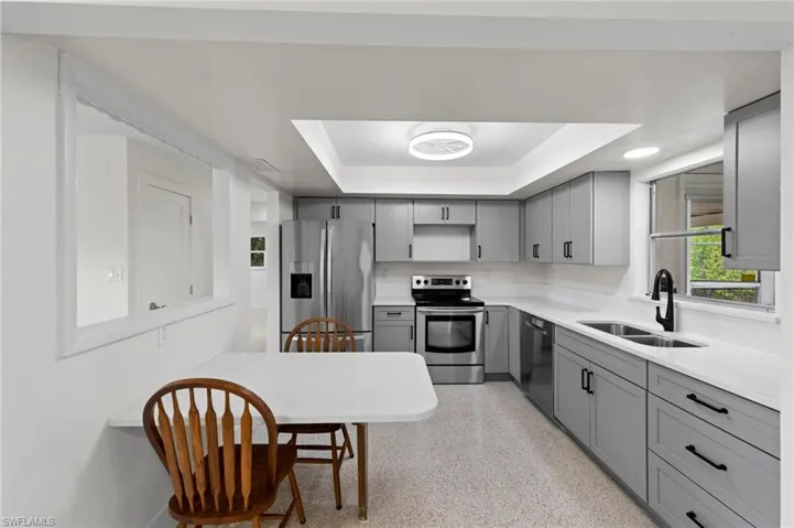 Kitchen featuring gray cabinetry, a raised ceiling, stainless steel appliances, and light stone counters