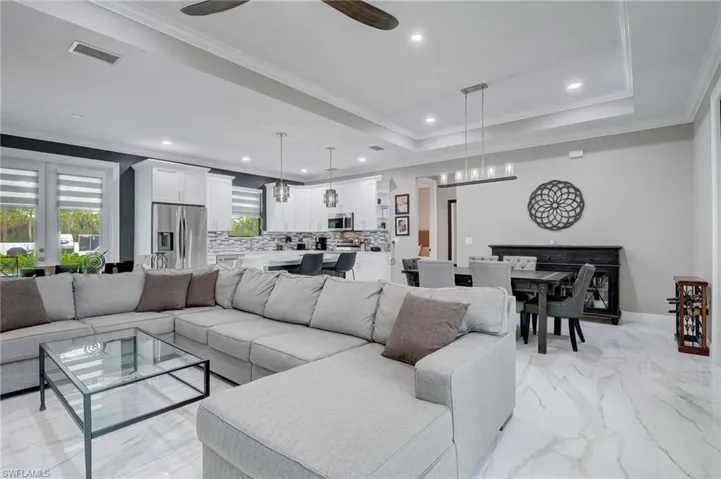 Living room with ceiling fan, a raised ceiling, crown molding, and light tile floors