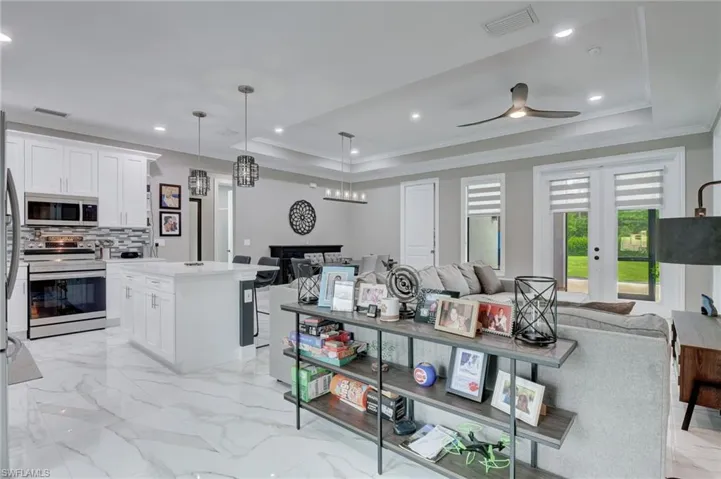 Kitchen with hanging light fixtures, a tray ceiling, range with electric stovetop, ceiling fan, and light tile floors