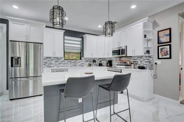 Kitchen with hanging light fixtures, appliances with stainless steel finishes, tasteful backsplash, and light tile flooring