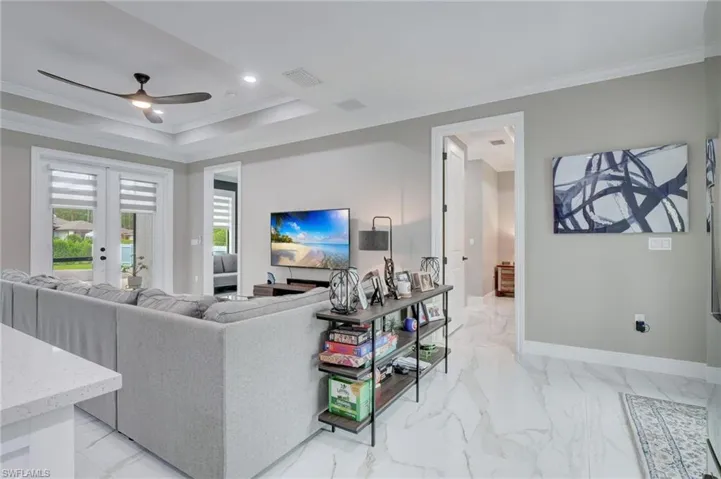 Living room with a raised ceiling, ornamental molding, ceiling fan, and light tile floors