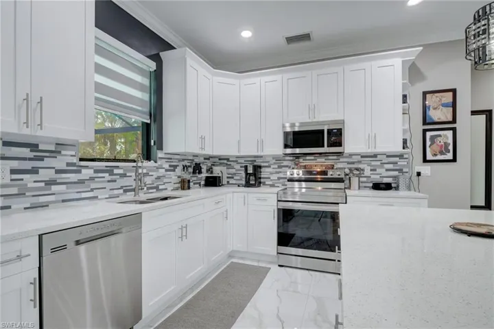 Kitchen with tasteful backsplash, white cabinetry, appliances with stainless steel finishes, sink, and light tile floors
