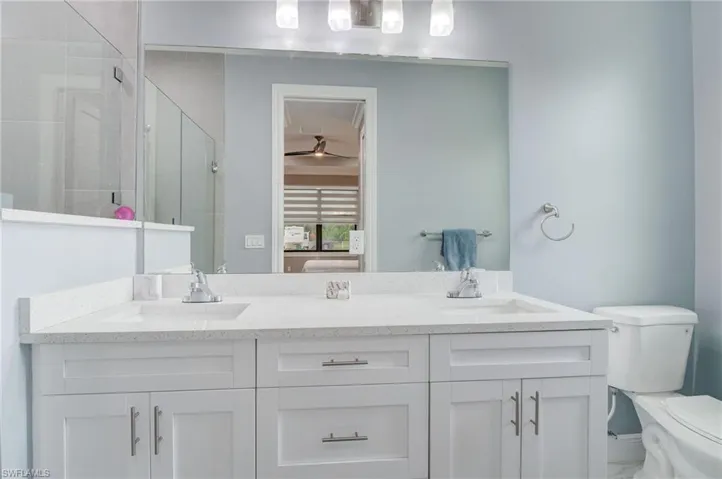 Bathroom with ceiling fan, double sink, a shower with door, toilet, and large vanity