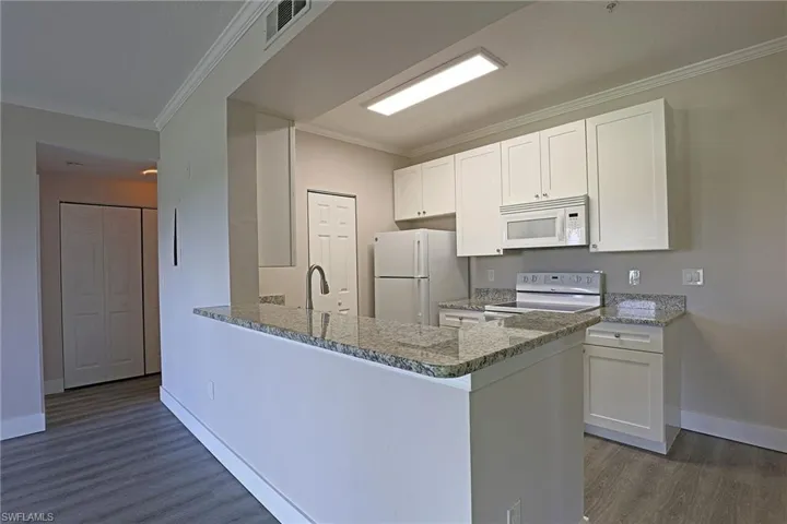 Kitchen featuring crown molding, white cabinets, dark stone countertops, white appliances, and a peninsula
