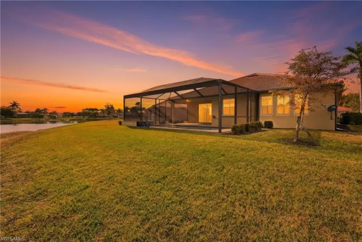 Back of house at dusk featuring glass enclosure, a lawn, a patio area, a sunroom, and a pool