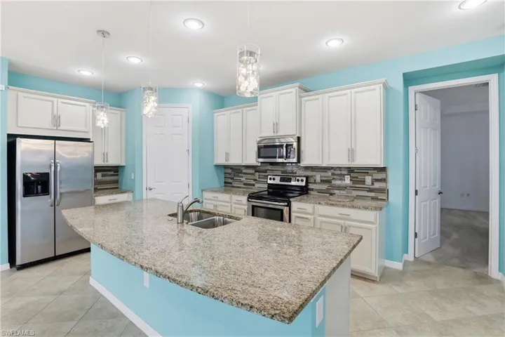 Kitchen with stainless steel appliances, white cabinets, hanging light fixtures, and light stone countertops