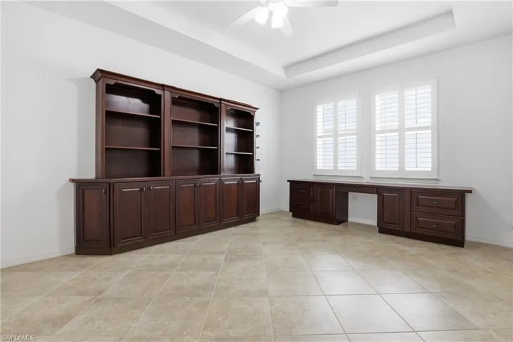 Unfurnished office with a raised ceiling, a ceiling fan, light tile patterned flooring, and built in study area