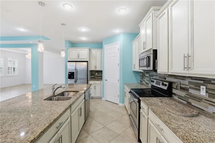 Kitchen with stainless steel appliances, light tile patterned floors, pendant lighting, and light stone countertops