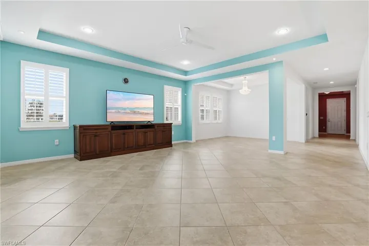 Unfurnished living room with a tray ceiling, a ceiling fan, light tile patterned floors, and recessed lighting