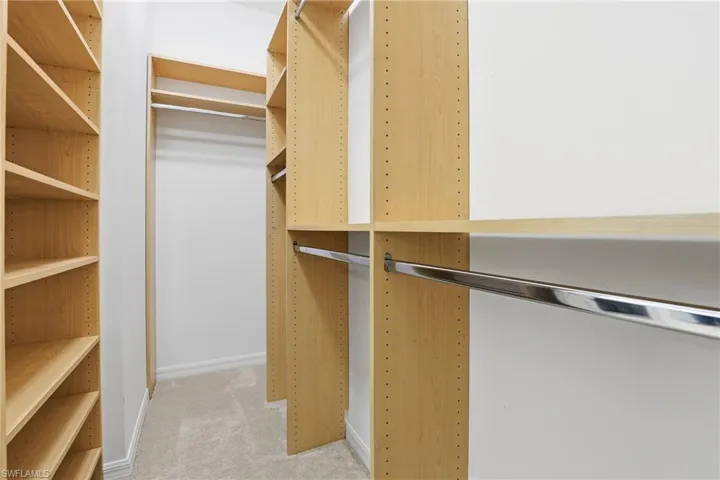 Primary bedroom walk in closet featuring light colored carpet