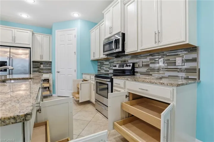 Kitchen with stainless steel appliances, light stone countertops, white cabinets, decorative backsplash, and light tile patterned floors