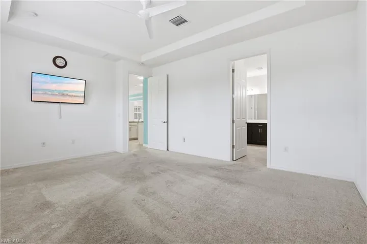 Unfurnished bedroom featuring a raised ceiling, light colored carpet, connected bathroom, and ceiling fan