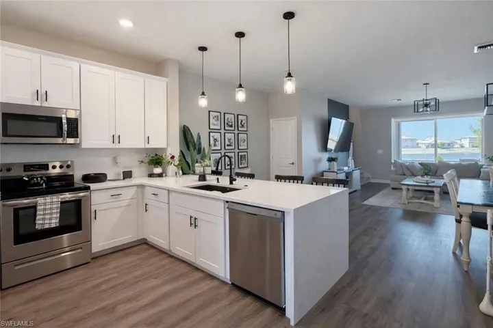 Kitchen featuring stainless steel appliances, a peninsula, white cabinets, and dark wood finished floors