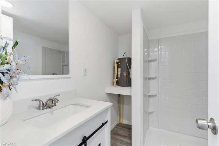 Full bath with vanity, electric water heater, a shower stall, and light wood-style floors