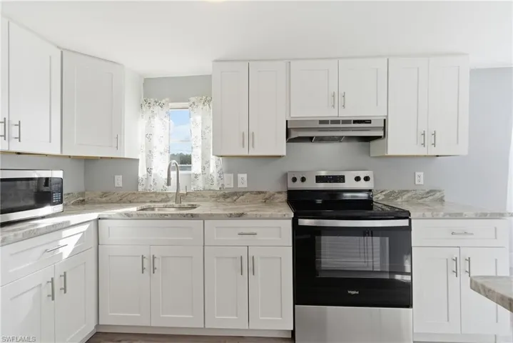Kitchen with stainless steel appliances, white cabinets, under cabinet range hood, and light stone countertops