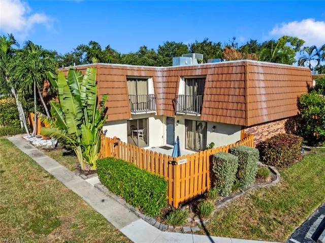 View of property featuring a balcony, a fenced front yard, mansard roof, and stucco siding