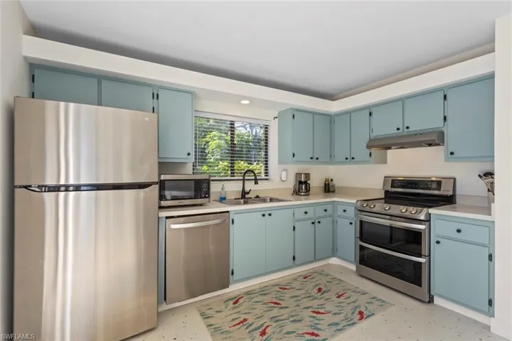 Kitchen with stainless steel appliances, light countertops, blue cabinetry, under cabinet range hood, and recessed lighting