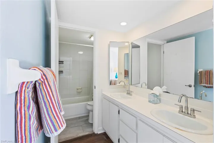 Primary Bathroom with dark wood-type flooring, double vanity, shower / bath combination, and recessed lighting