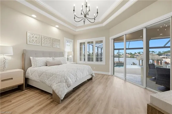 Extra large primary bedroom with tray ceiling, elegant chandelier, and updated flooring. Triple slider looks out to Lanai with expansive water views and quick access for a night time dip in the pool or spa.