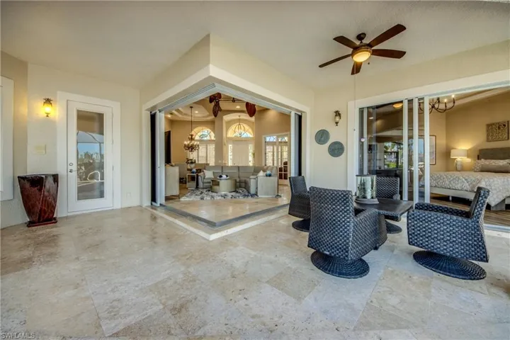 Covered and elevated Lanai area with Key West Travertine decking and outdoor dining. 2 sets of triple Pocketing 90 degree sliders into Great room and also triple sliders into Primary bedroom. Easy access Door to Pool Bathroom