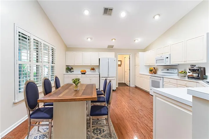Kitchen with white appliances, lofted ceiling, a kitchen breakfast bar, light wood-style floors, and white cabinets