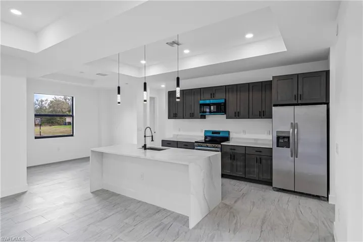 Kitchen featuring a raised ceiling, stainless steel appliances, light stone countertops, pendant lighting, and a kitchen island with sink