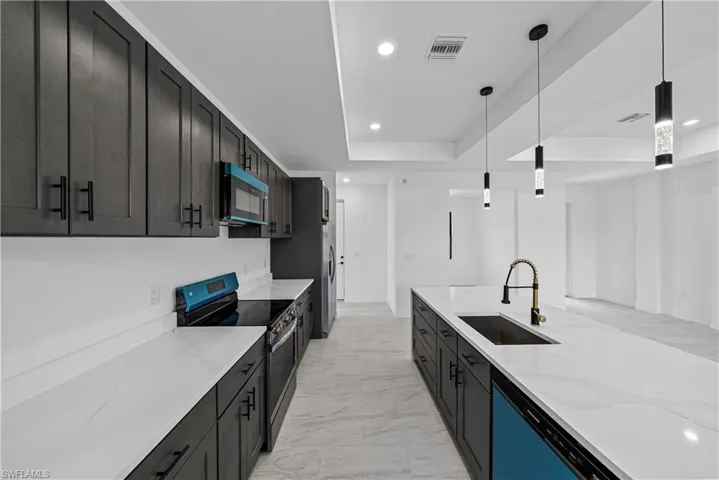 Kitchen featuring stainless steel range with electric cooktop, light stone counters, a raised ceiling, decorative light fixtures, and dishwasher
