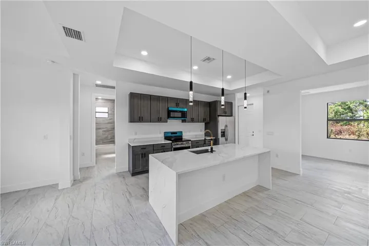 Kitchen featuring light stone countertops, stainless steel appliances, a tray ceiling, dark wood finish cabinetry, and hanging light fixtures