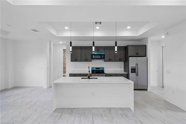 Kitchen featuring a tray ceiling, light stone countertops, stainless steel appliances, decorative light fixtures, and dark wood finish cabinets