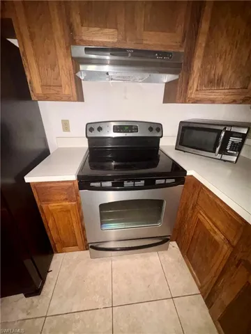 Kitchen featuring stainless steel appliances, wood finish cabinetry, light countertops, and light tile patterned floors