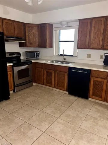Kitchen with black appliances, light countertops, and light tile patterned flooring