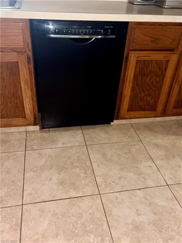 Kitchen view of black dishwasher, wood finish cabinetry, and light countertops