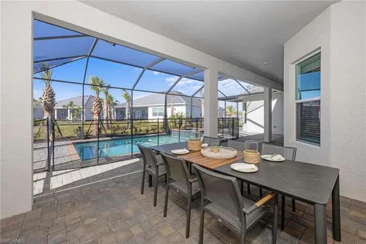 View of patio with outdoor dining space, a pool with connected hot tub, and a lanai