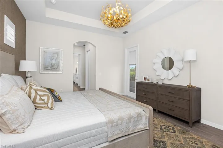 Bedroom featuring arched walkways, a tray ceiling, a chandelier, and wood finished floors