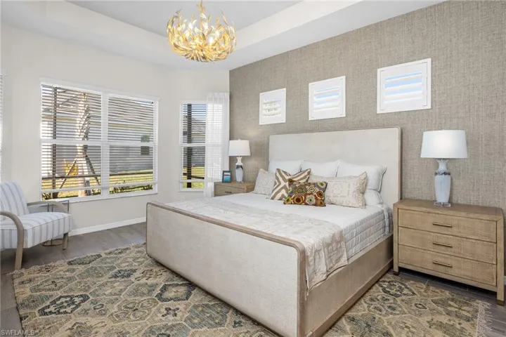 Bedroom with a raised ceiling, a chandelier, wood finished floors, an accent wall, and wallpapered walls